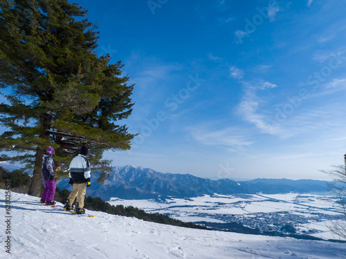 Snowboarders looking over snow covered town from a ski slope on a sunny day (Inawashiro, Fukushima, Japan)