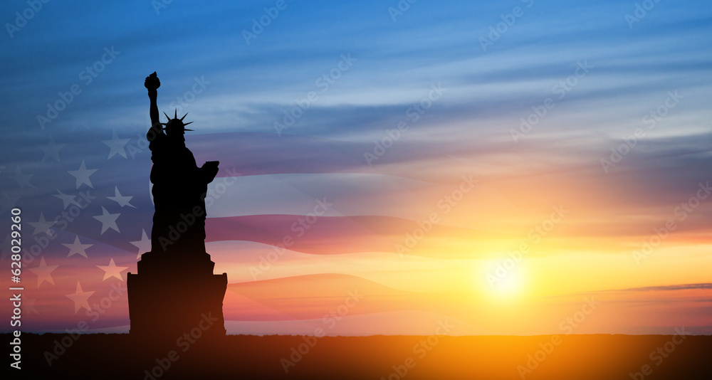 Statue of Liberty with american flag on background of sunset sky.