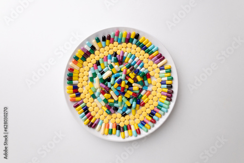 A large number of multi-colored pills lay on a white plate. And there are chopsticks placed beside the plate.