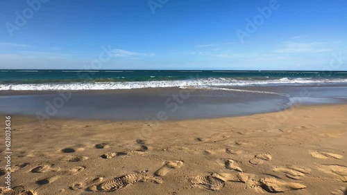 waves roll onto beach with sandy footsteps in the foreground photo