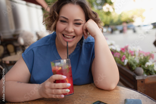 Beautiful young woman sit in cafe with glass of cooly drink. Plus size woman  drink red juice and smiling