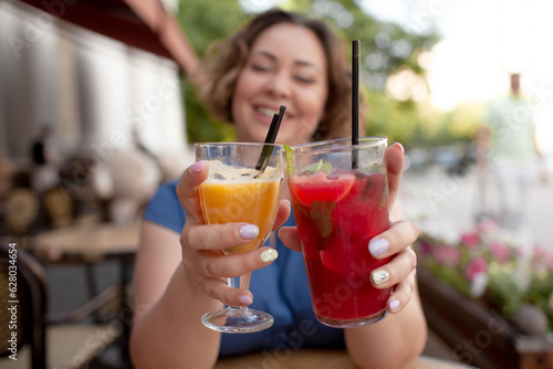 Beautiful young woman sit in cafe with glass of cooly drink. Plus size woman drink red juice and smiling