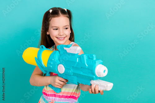 Photo of cheerful funky cute girl wear striped stylish clothes shooting water gun looking empty space isolated on blue color background