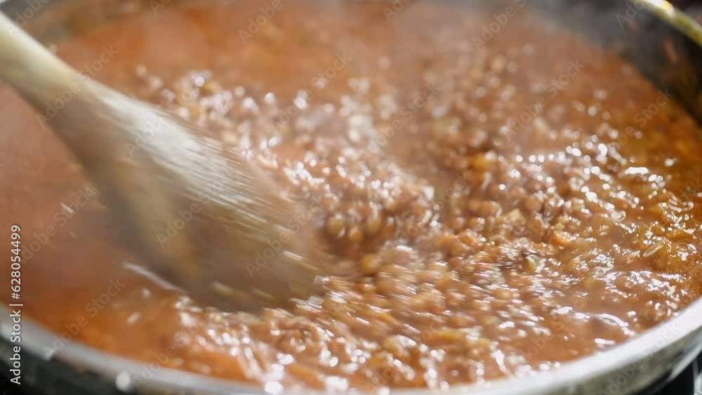 The cook prepares lentils stew in the pan.
The cook prepares lentils stew in the pan.