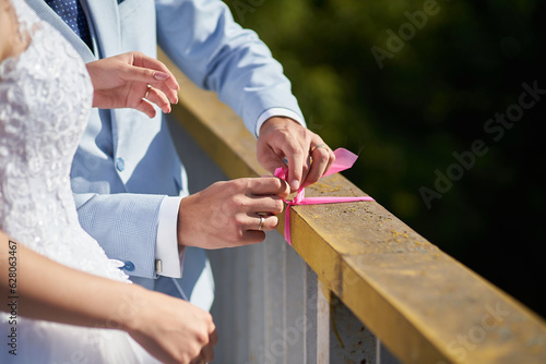 Close-up of newlyweds tying a ribbon on a bridge railing
