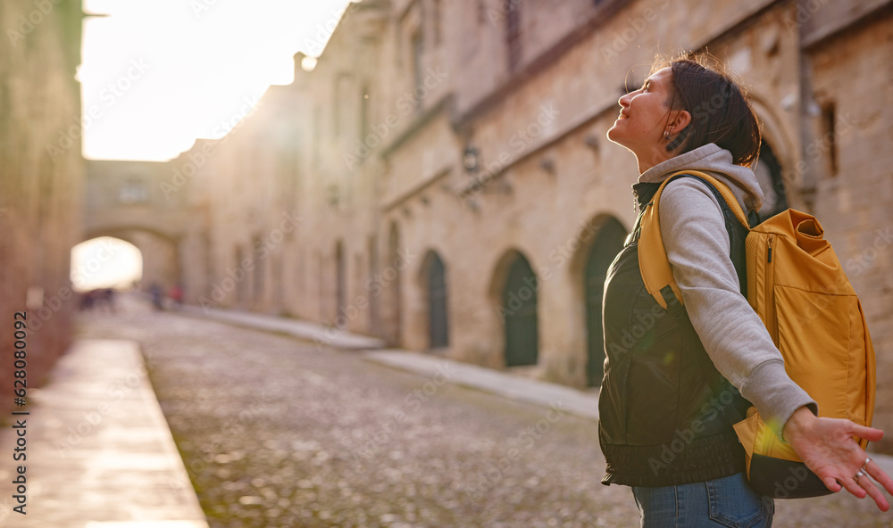 spring or fall trip to Rhodes island, Greece. Young Asian woman walks Street of Knights of Fortifications castle over sunset time. female traveler visiting southern Europe. Unesco world heritage site.