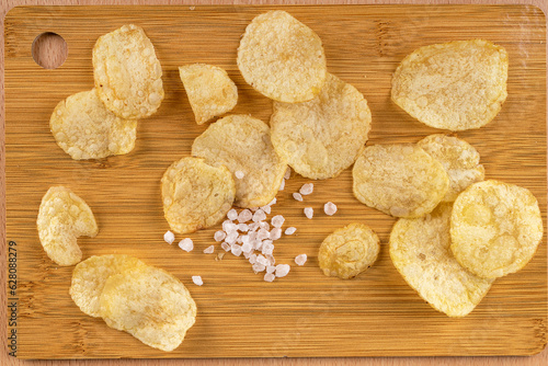 Top view of crispy salted potato chips on a cutting board. © svdolgov