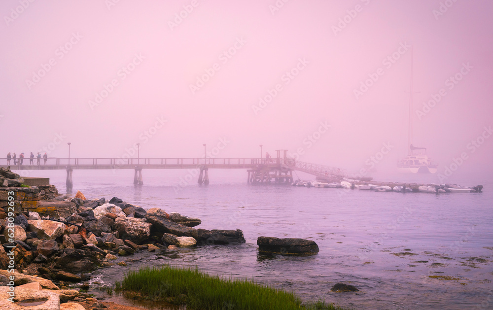 Misty sunrise seascape on a foggy morning at Boothbay Harbor with the view of Footbridge and moored ships in Lincoln County, Maine