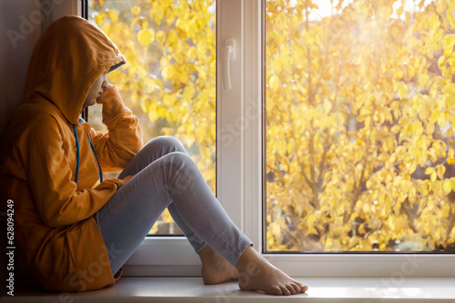 Depressed Stressed Teenager Girl in Autumn Window Sill. Difficult Adolescent Depressed. Sad Alone Teen with Negative  Pesimistic Mood on Yellow Background photo
