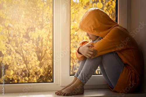 Depressed Unhappy Teenage Girl  by Window Alone, feeling Lonely. Autumn Depression. Stressed Sad teenager thinking about Troubles, Psychological problem. © Maryana