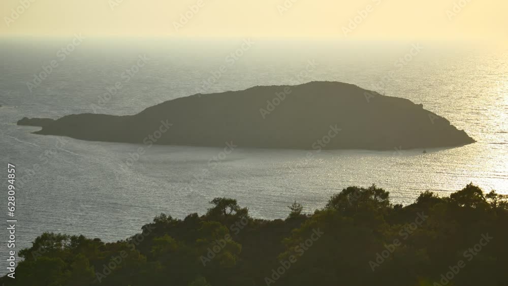 Mediterranean island and golden water surface with the waves glittering in the sun. Sea landscape with rocky island and the sunrise. Blinking particles of golden sun lights on the sea surface Mediterranean island and golden water surface with the waves glittering in the sun. Sea landscape with rocky island and the sunrise. Blinking particles of golden sun lights on the sea surface