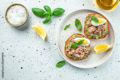 bread toast with tuna, avocado and boiled egg on light background. Healthy appetizer, breakfast, lunch or snack. banner, menu, recipe place for text, top view