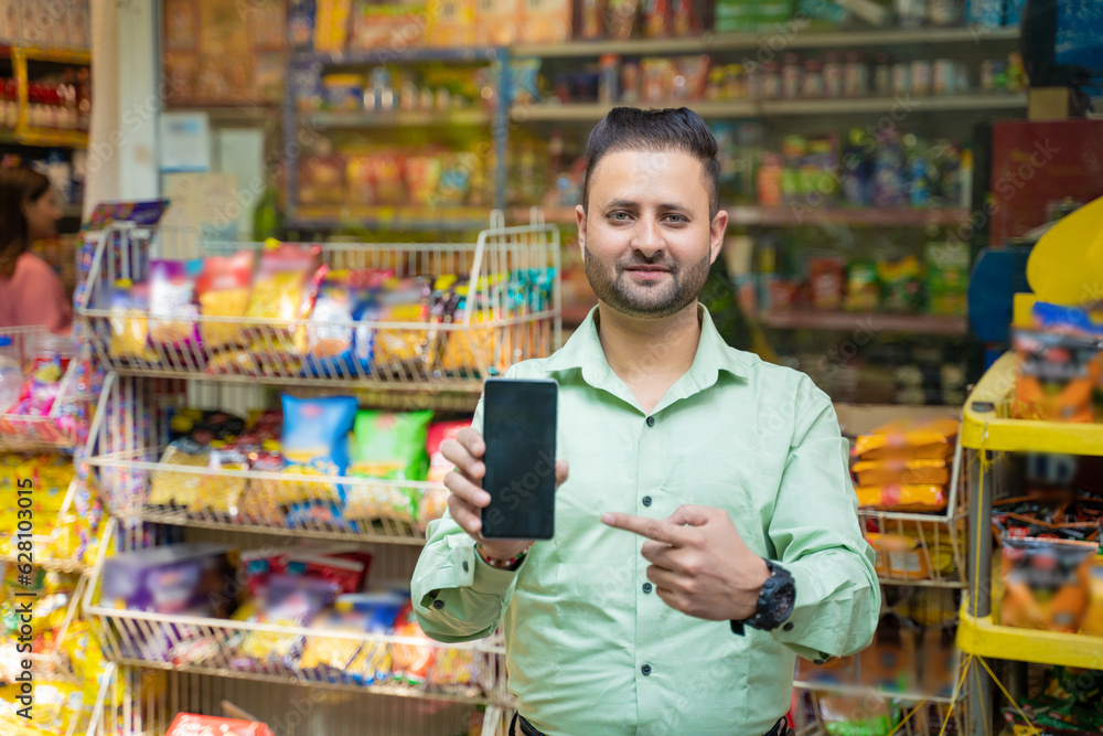 Young indian man showing smartphone screen at grocery shop.