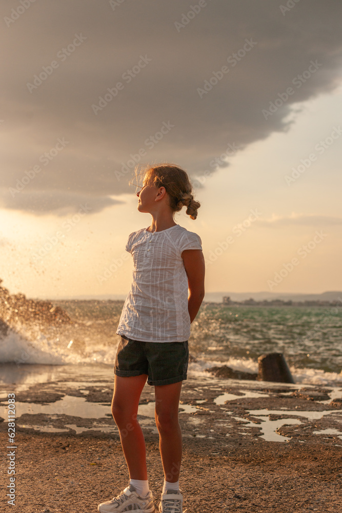 A girl stands on the shore of a troubled sea before the rain. Relax and enjoy the sound of the surf