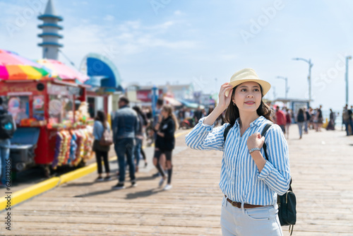 smiling asian chinese woman traveler looking at beautiful scenery at santa monica pier with street food stands at background
