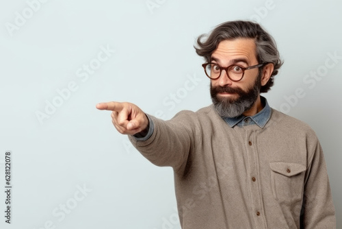 Bearded man with glasses pointing to blank space on orange background