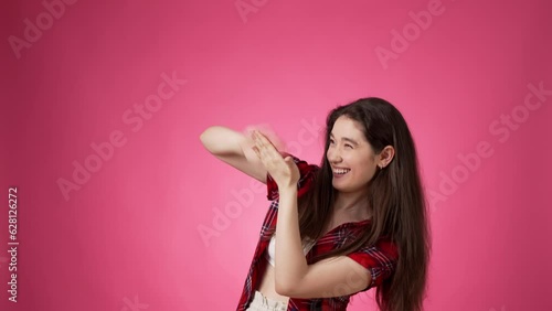 Casually dressed young brunette making money gestures while suggestively smiling and using expressive body language against pink background photo