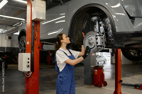 Woman mechanic fixing wheel hub or disc brake of raised car on lift mechanism
