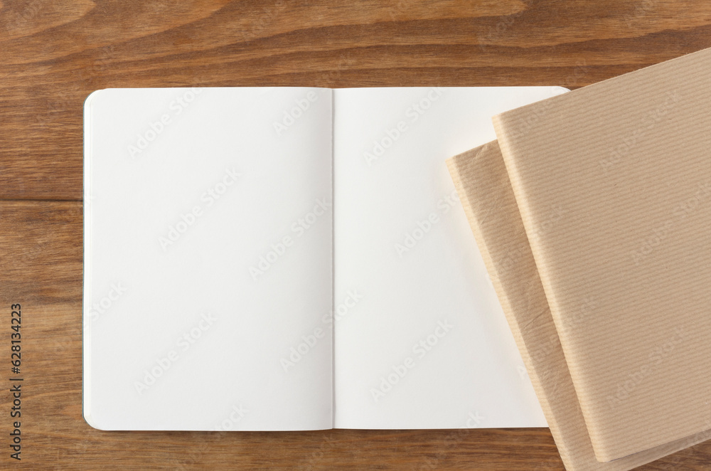 Blank notebook with spread and two books on wooden desk Blank notebook with spread and two books on wooden desk