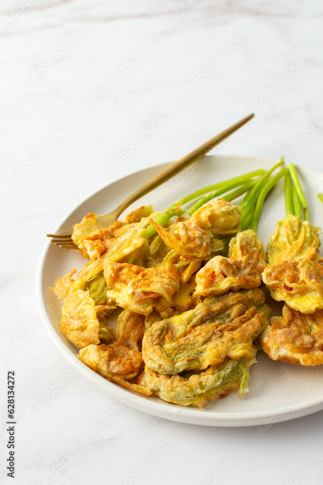 Fried zucchini flowers in batter, plate with zucchini flowers on marble background Fried zucchini flowers in batter, plate with zucchini flowers on marble background