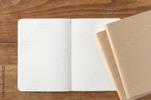 Blank notebook with spread and two books on wooden desk
