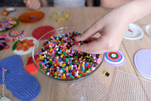 close-up of children's hands creating perler bead patterns, make crafts using thermomosaic technique, beading patterns, perler bead art, concept development of fine motor skills, thermo mosaic ideas photo