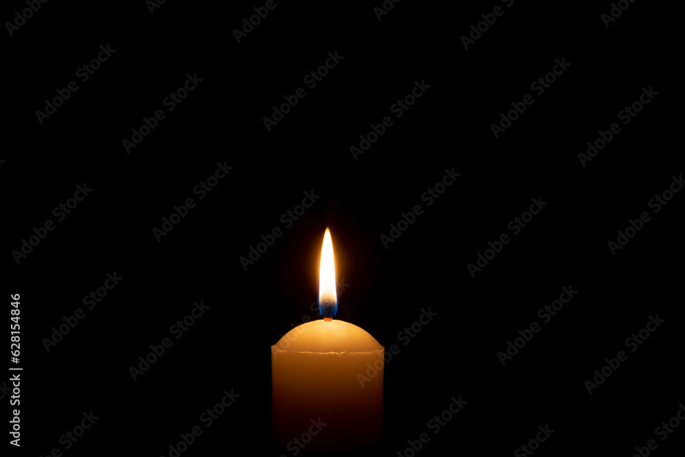 Single burning candle flame or light glowing on a big white candle on black or dark background on table in church for Christmas, funeral or memorial service with copy space. Single burning candle flame or light glowing on a big white candle on black or dark background on table in church for Christmas, funeral or memorial service with copy space.