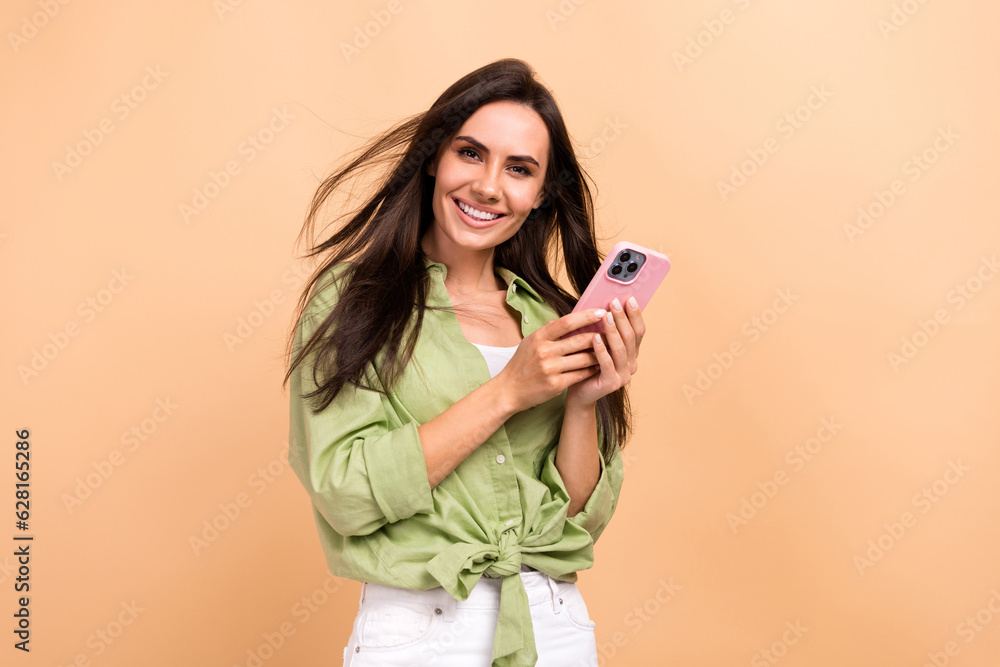Photo of gorgeous girl straight hairstyle dressed green blouse hold smartphone get income notification isolated on beige color background Photo of gorgeous girl straight hairstyle dressed green blouse hold smartphone get income notification isolated on beige color background