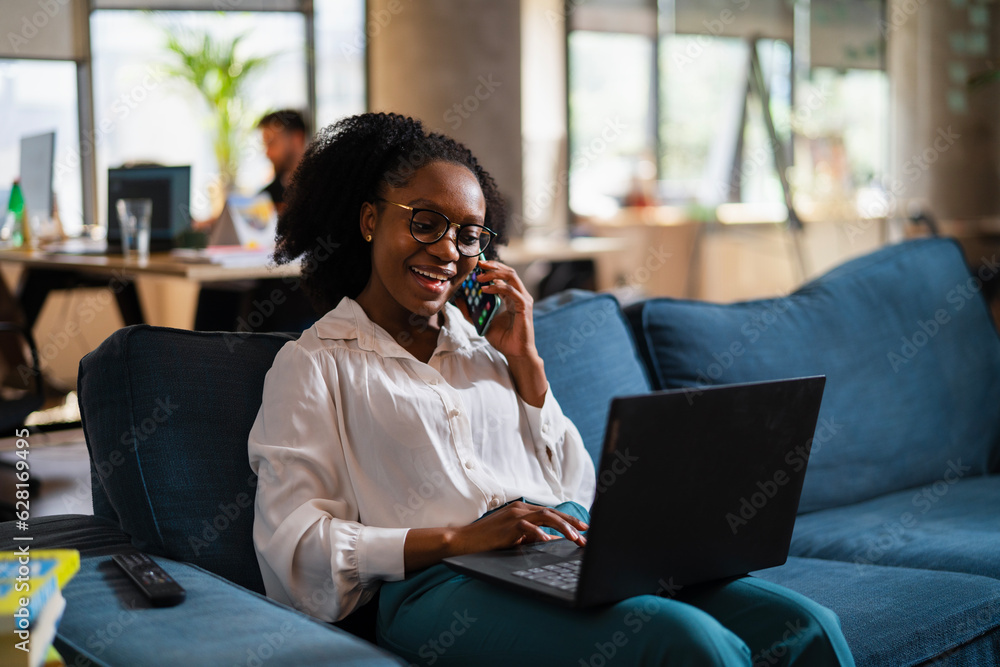 Black businesswoman working on laptop. Portrait of beautiful businesswoman talking to the phone in the office..