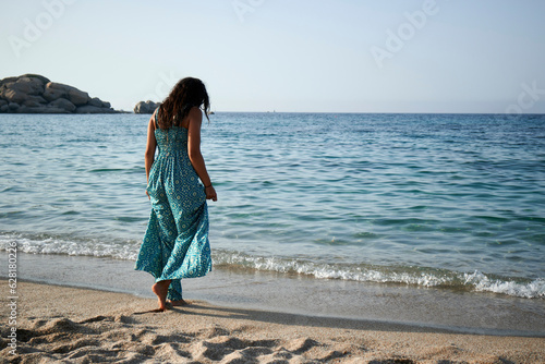 A beautiful young woman walking on the beach wearing a blue dress