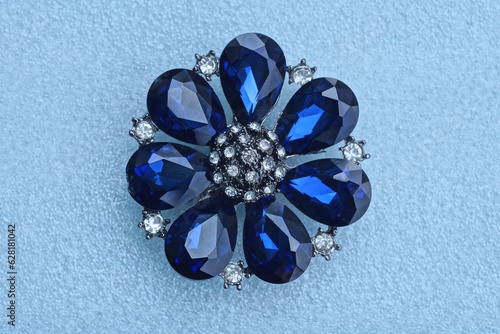 one round silver jewelry brooch in the shape of a flower with  blue stones lies on a white table photo