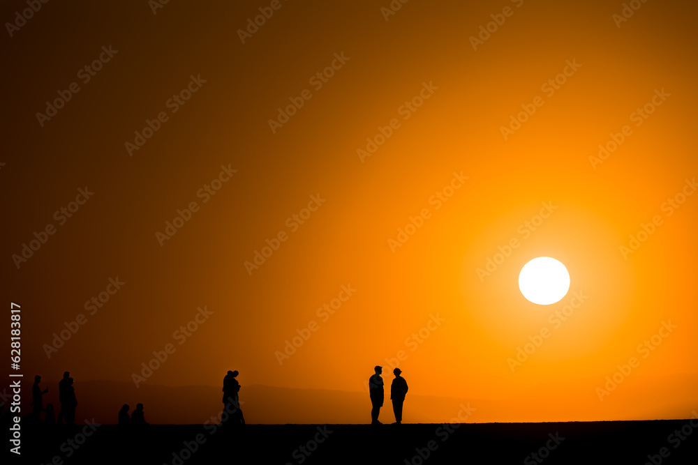 Fototapeta premium Silhouette of tourists watching a spectacular sunset from a harbour wall (Chania, Crete, Greece)
