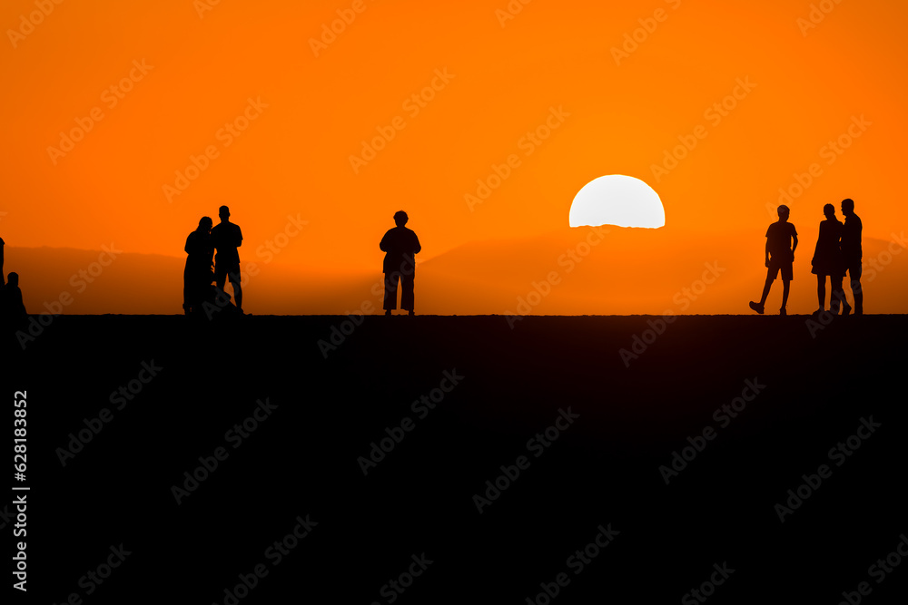 Silhouettes of people watching the sun set behind a distance mountain from a sea wall (Chania, Crete, Greece)