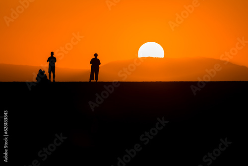 Silhouettes of people watching the sun set behind a distance mountain from a sea wall  Chania  Crete  Greece 