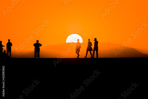 Silhouette of tourists watching the sun set behind a distant mountain in summer