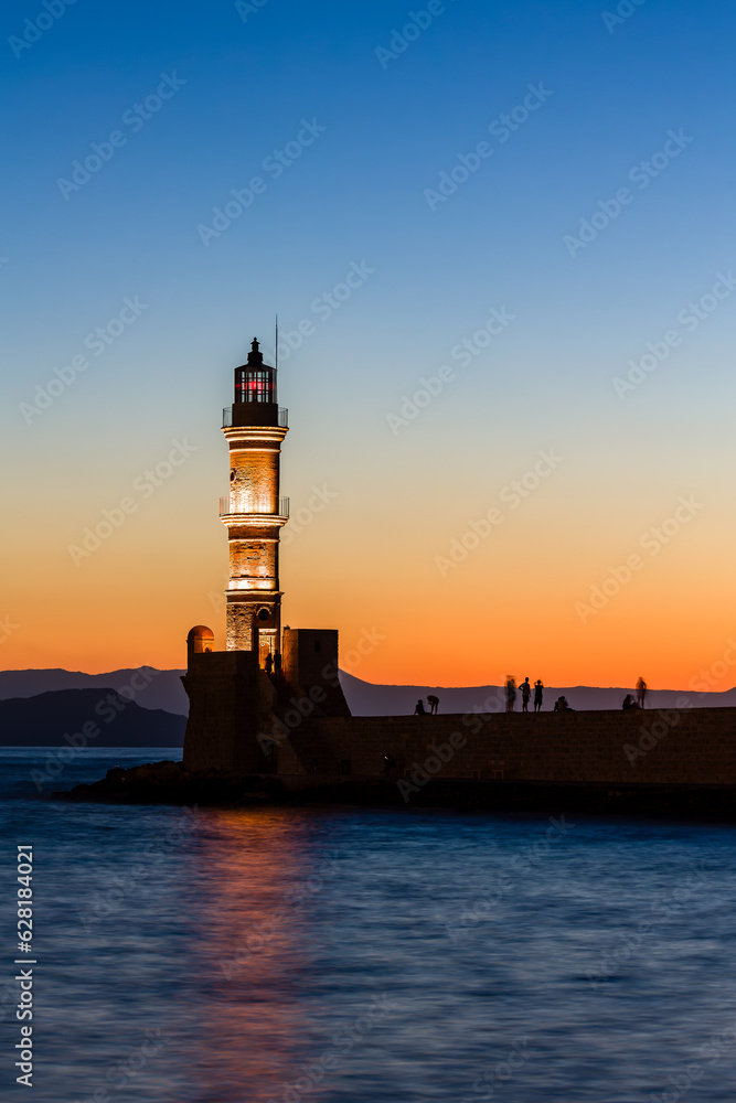 Long exposure, blurred image of an old lighthouse at sunset with watching tourists in silhouette
