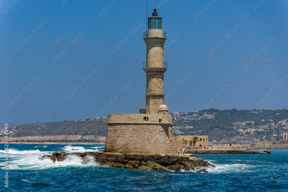 Waves breaking on a sea wall next to an old Venetian era lighthouse on a clear day