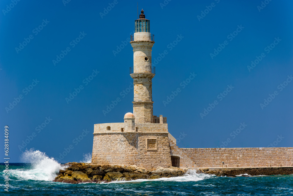 Waves breaking on a sea wall next to an old Venetian era lighthouse on a clear day