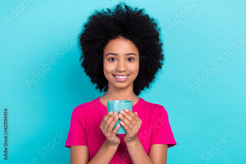 Photo of satisfied cheerful girl with afro chevelure wear pink t-shirt hands hold cup of hot tea isolated on blue color background
