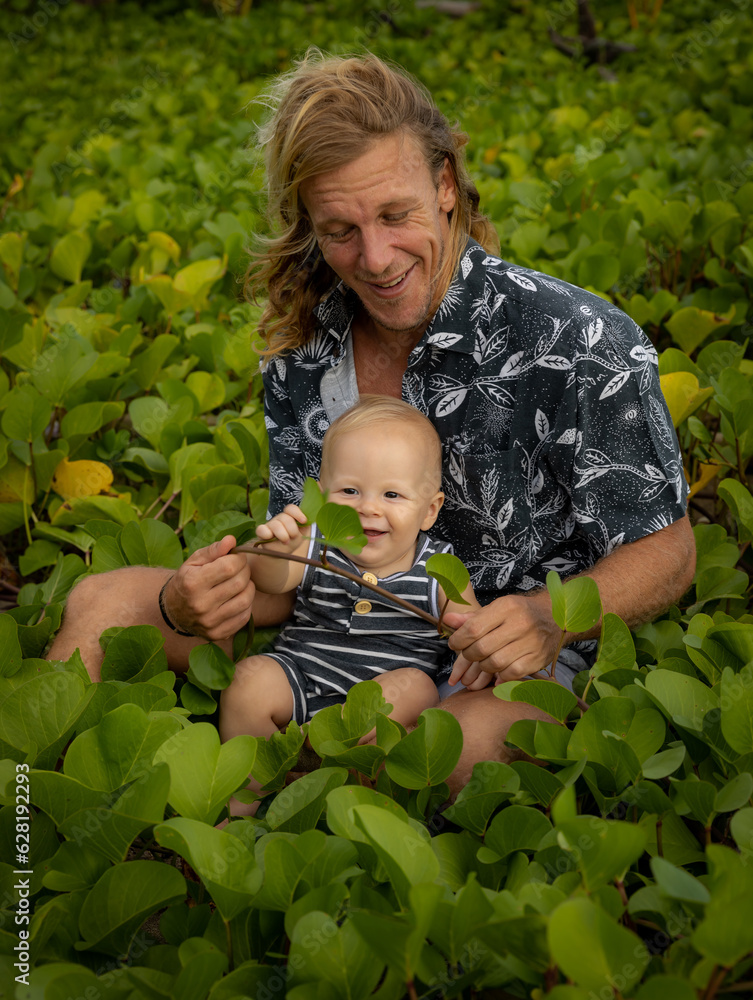 Young father with baby infant boy spending time in nature. Outdoor activities. Dad and baby boy sitting on the ground. Smiling kid. Background of green leaves. Happy childhood. Bali Young father with baby infant boy spending time in nature. Outdoor activities. Dad and baby boy sitting on the ground. Smiling kid. Background of green leaves. Happy childhood. Bali