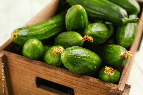 Box with fresh cucumbers on light wooden background, closeup