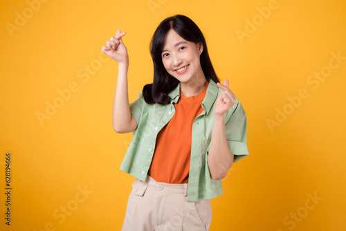 young Asian woman in her 30s dressed in an orange shirt and green jumper. Her mini heart gesture and gentle smile speak volumes of affection and happiness. body language concept.