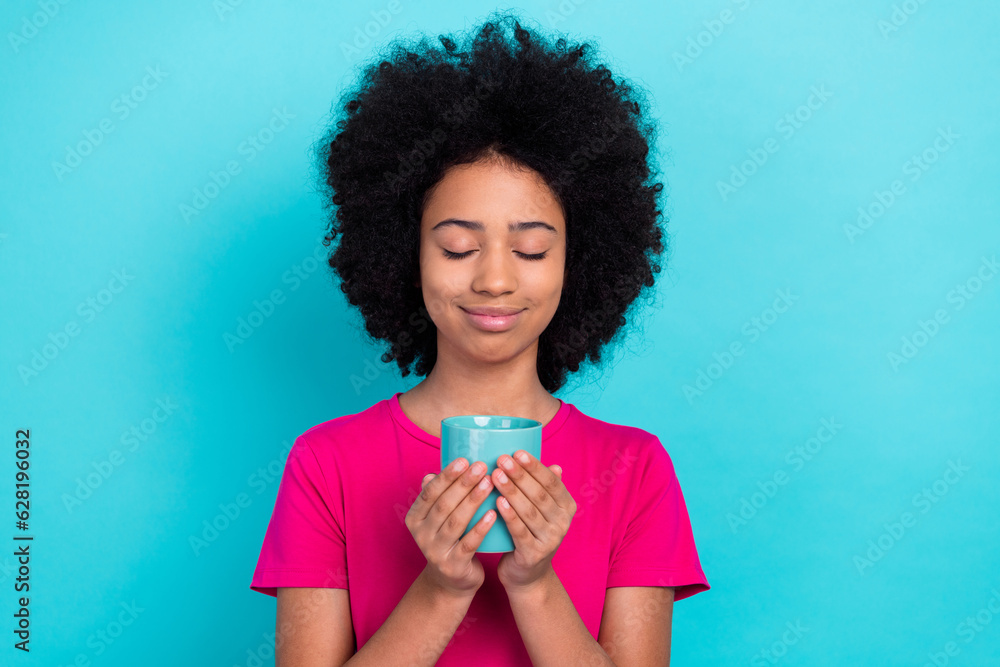 Photo of satisfied adorable girl with afro chevelure wear pink t-shirt hands holding cup of cacao isolated on blue color background Photo of satisfied adorable girl with afro chevelure wear pink t-shirt hands holding cup of cacao isolated on blue color background