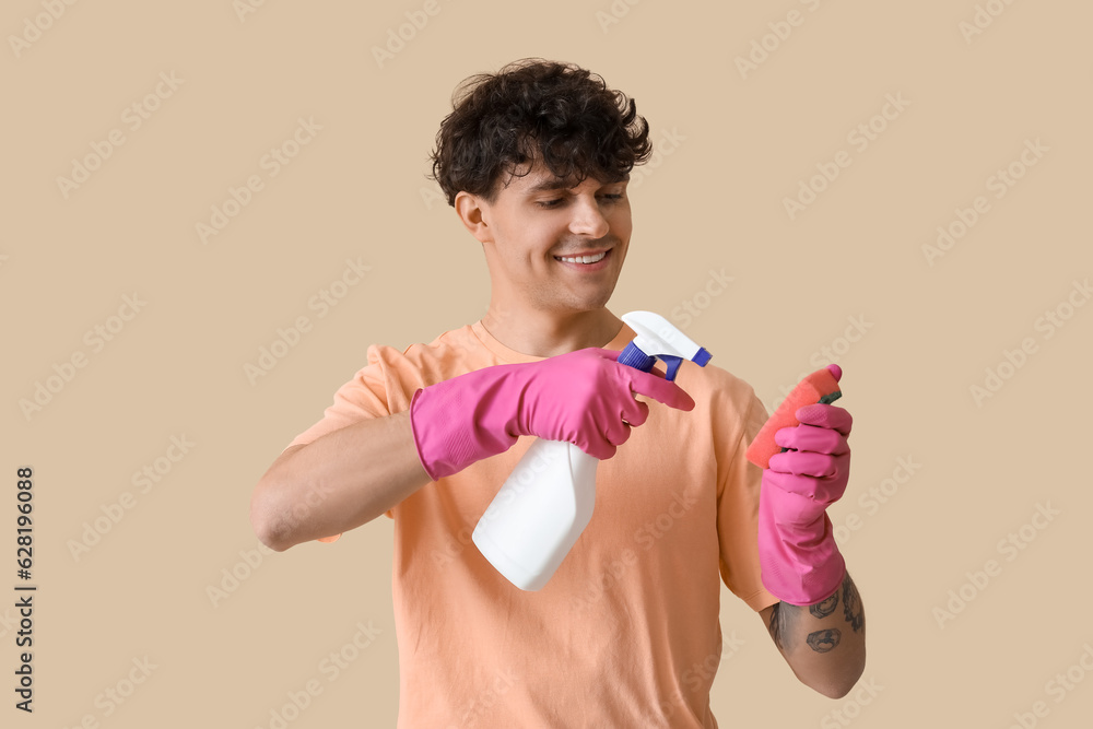 Young man with detergent and cleaning sponge on beige background