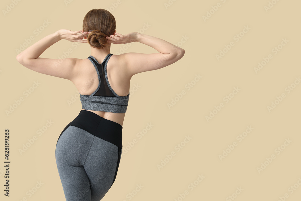 Obraz premium Young woman in sportswear on beige background, back view
