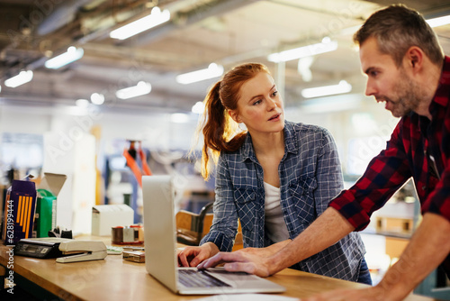 Young man and young woman using a laptop while working in a printing press office