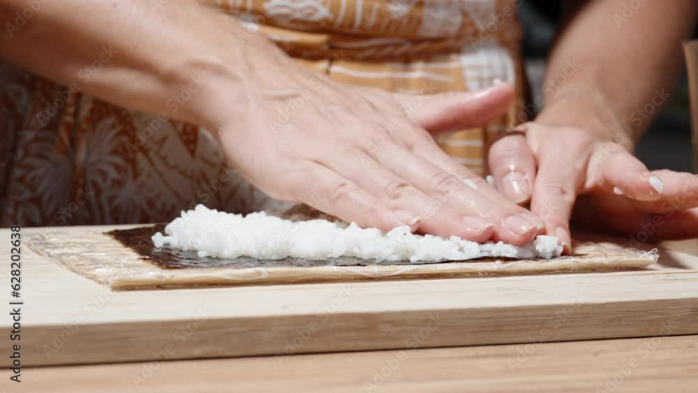The woman spreads rice on the dry nori seaweed sheets using bamboo sticks. The woman spreads rice on the dry nori seaweed sheets using bamboo sticks.