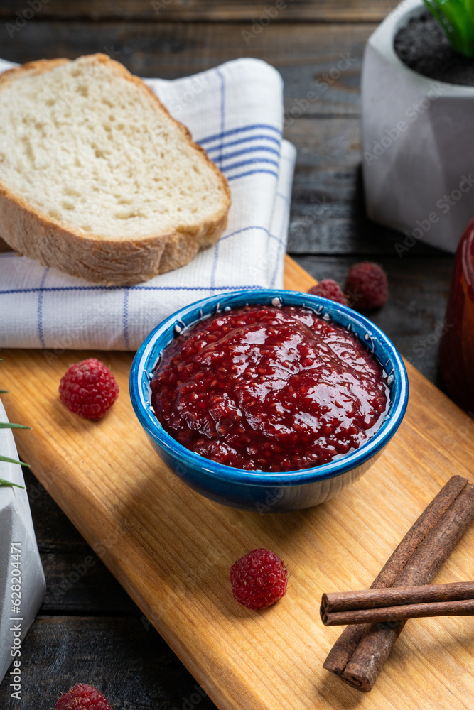 Fresh homemade raspberry jam in a bowl served on a wooden platter with bread