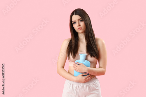 Young woman with hot water bottle having menstrual cramps on pink background photo