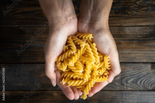 Εκτύπωση καμβά Raw uncooked Italian pasta fusilli held in two hands over a dark wooden backgrou